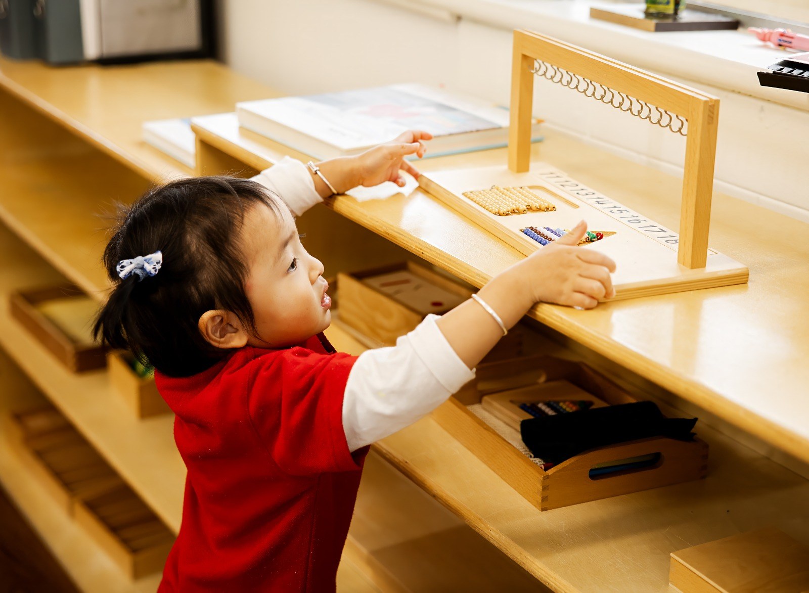 A child reaching for a material on the classroom shelf