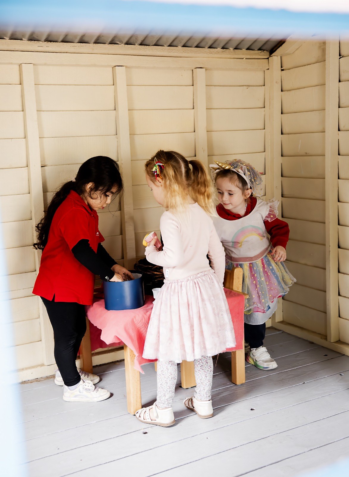 An educator and children at a table during outdoor pretend play