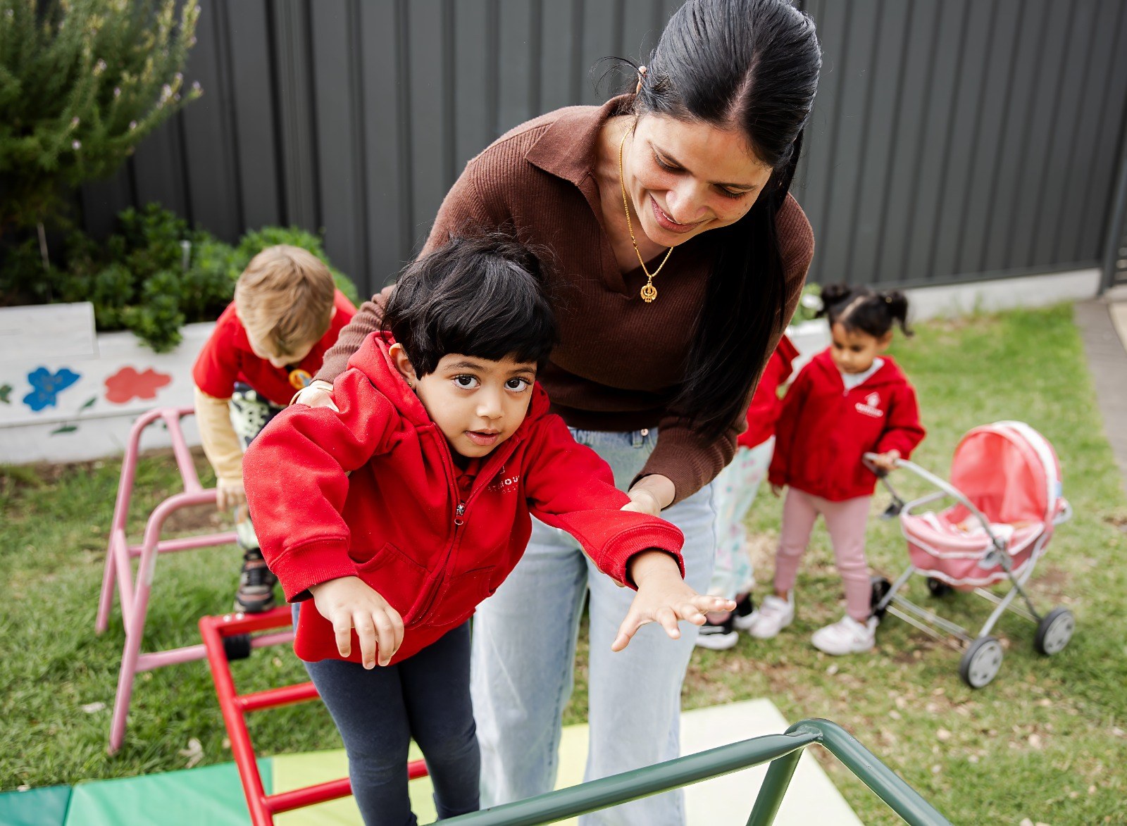 An educator supporting a child on the outdoor balance beam