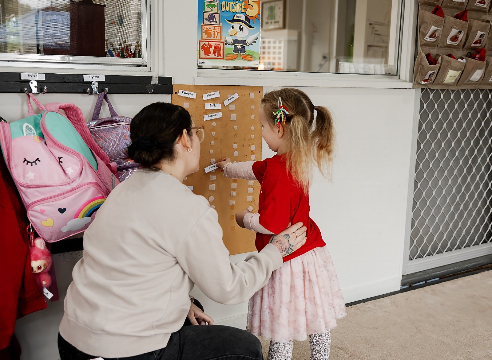 An educator and child at a classroom wall chart