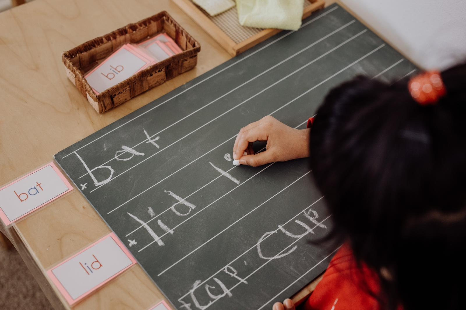Child writing words with sandpaper letters and word cards